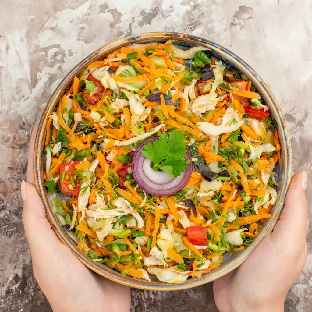 Fresh vegetarian salad with shredded carrots, cabbage, tomatoes, green herbs, and onion slices served in a rustic bowl.