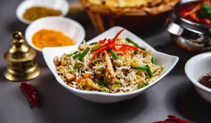 Indo-Chinese fried rice with vegetables and chicken served in a white bowl, garnished with spring onions and red chilies.