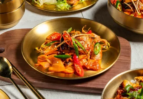 Indo-Chinese food served in brass bowls with stir-fried vegetables, red and green chilies, and golden cutlery on a wooden board.