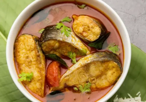 Kerala curry with fish pieces in spicy red gravy garnished with curry leaves and coriander.