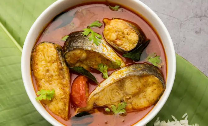 Kerala curry with fish pieces in spicy red gravy garnished with curry leaves and coriander.