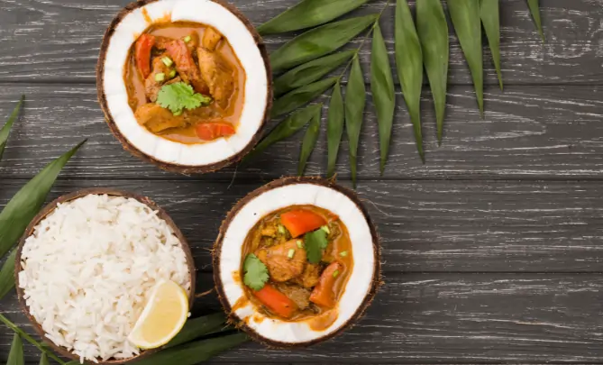 Kerala curry in bowls served with steamed white rice, lemon slice, and fresh curry leaves on a wooden table.