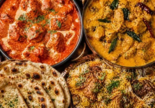 Overhead view of an Indian banquet table with butter chicken, Kerala coconut curry, mutton biryani, and assorted breads shared among a group